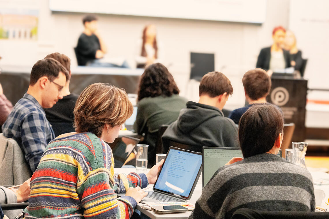 Personen sitzen am Tisch vor Laptops