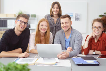 Symbolbild: 5 Studierende sitzen an einem Tisch mit Laptop und Lernunterlagen