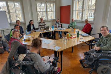 Personen sitzen am Tisch und lächeln in Kamera