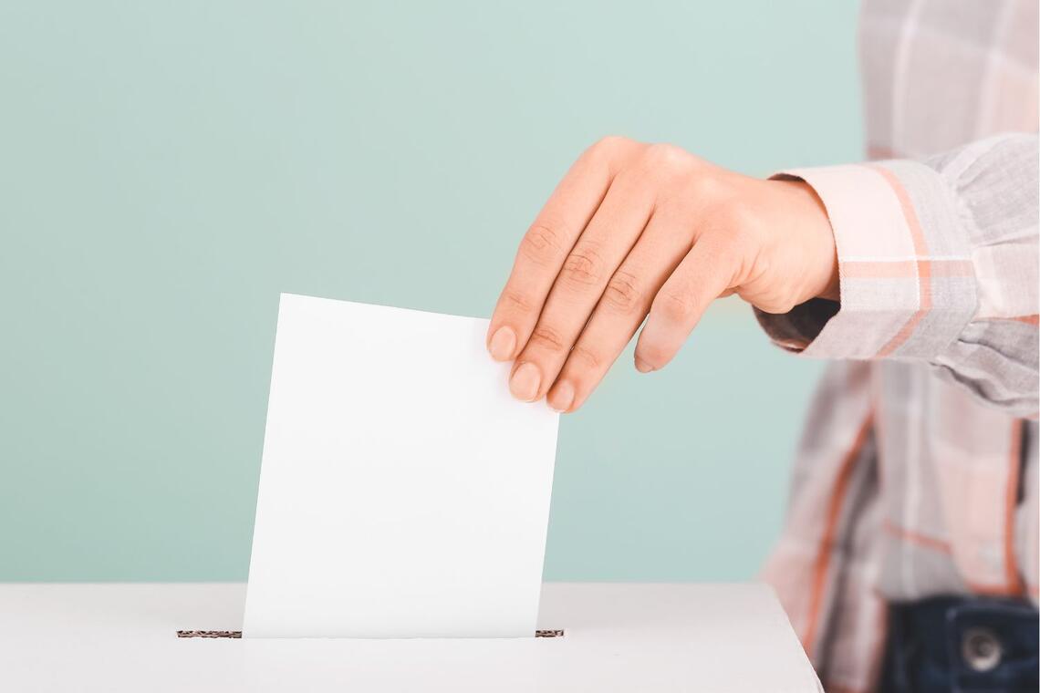 Hand steckt Wahlkuvert in Wahlurne