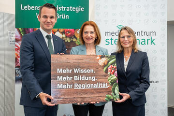 Zwei Frauen und ein Mann stehen nebeneinander und halten eine Tafel in ihren Händen