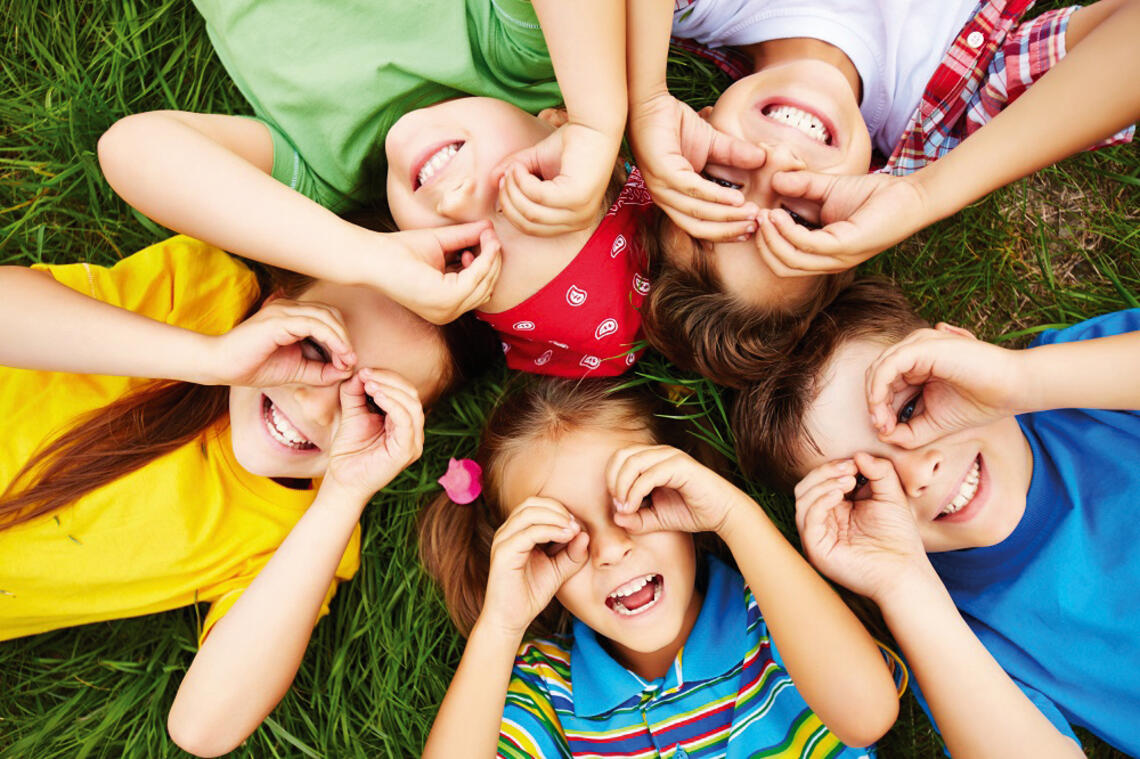 Fünf Kinder liegen in einer Wiese