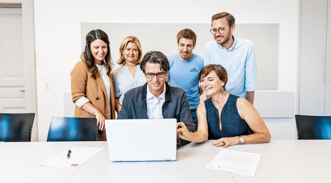 Personen versammeln sich um einen Laptop und schauen darauf 