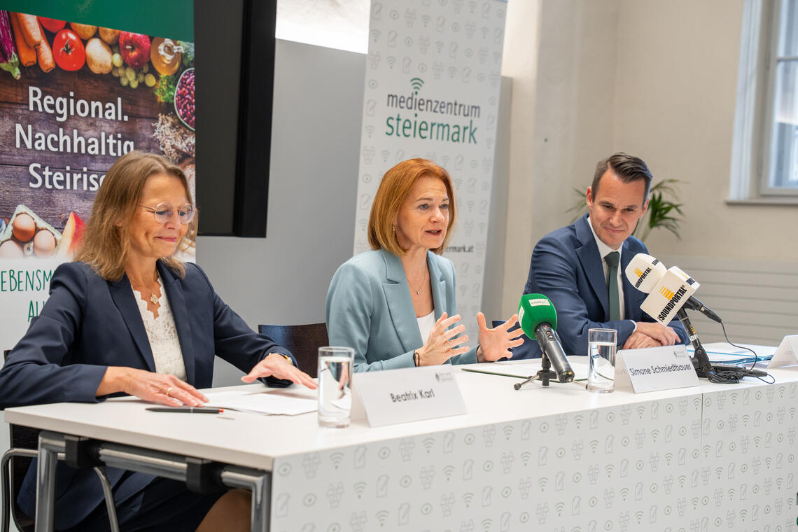 Zwei Frauen und ein Mann sitzen während einer Pressekonferenz nebeneinander an einem Tisch